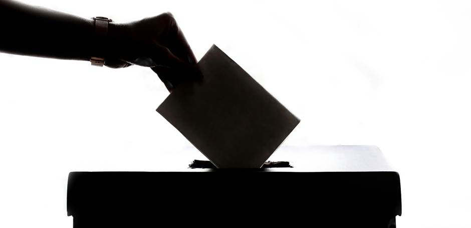 A hand placing a ballot into a box
