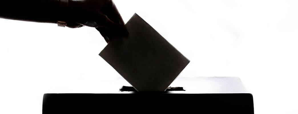 A hand placing a ballot into a box
