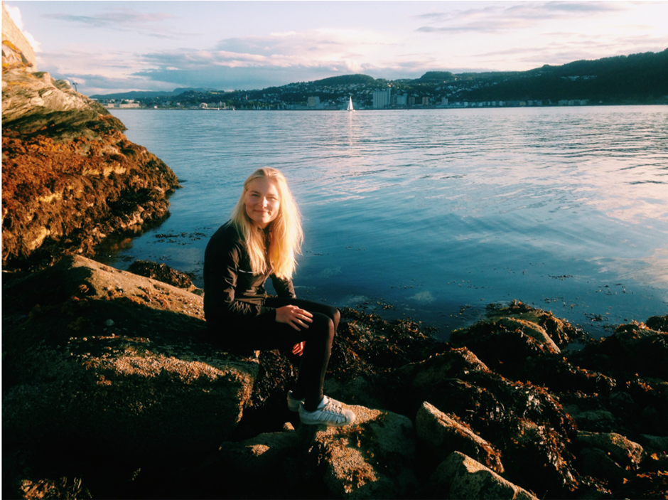 Jente sitter på en sten med utsikt til havet