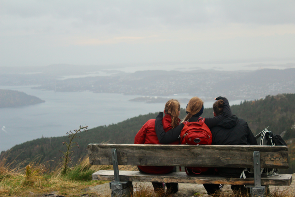 Tre jenter på en benk på toppen av et fjell som nyter utsikten