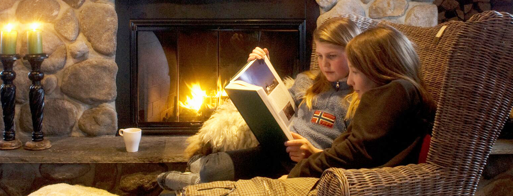 Two girls reaading a book in front of the fire place - Photo:Photo: CH/Innovation Norway